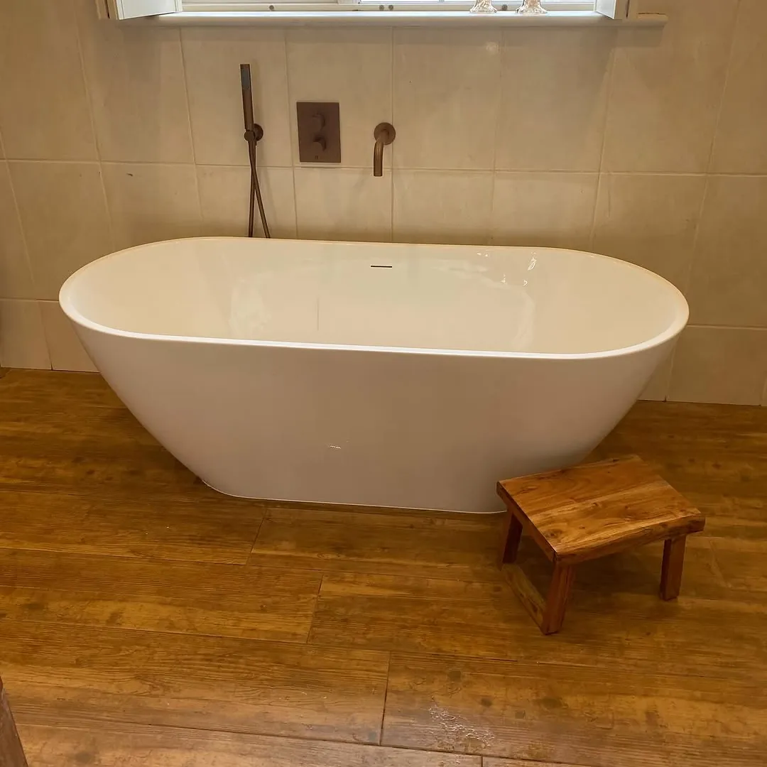 White freestanding bath with brushed copper wall taps and a wood-effect tiled floor