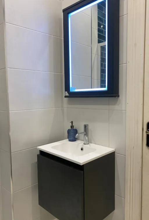 Small dark vanity unit under a lit mirror